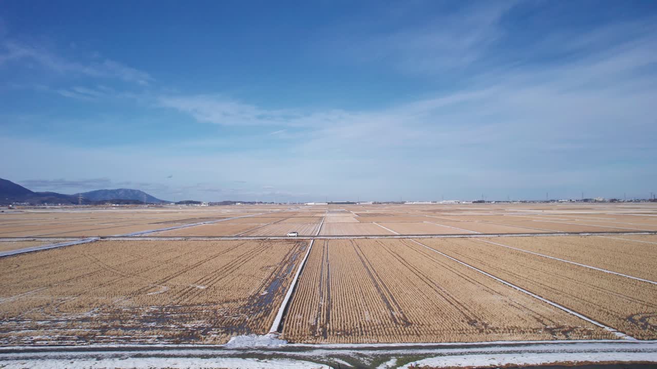 Smooth drone movement follows a vehicle traveling across agricultural land during winter in Japan