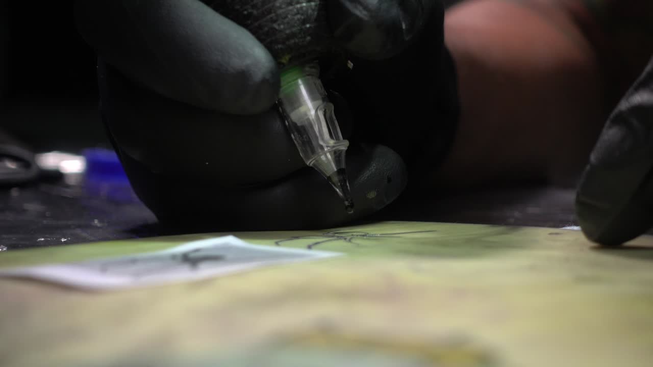 un tatuador carga agujas con tinta negra y completa un tatuaje en piel sintética