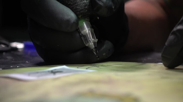 Un tatuatore carica gli aghi con inchiostro nero e completa un tatuaggio su pelle sintetica