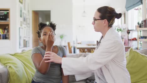 chica afroamericana y doctora caucásica sentada en el sofá en la sala de estar usando un inhalador