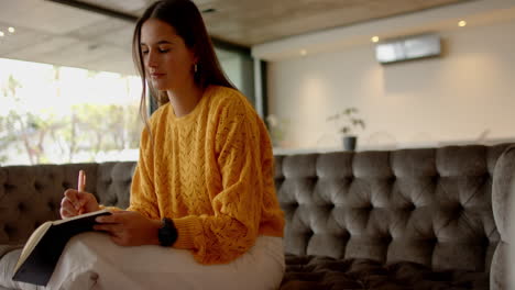 writing in notebook, woman sitting on sofa in cozy home environment