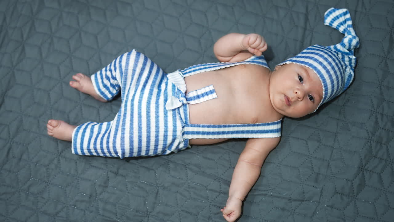 Sweet plump baby boy wearing blue and white costume. Full-length portrait of a toddler lying on grey background.