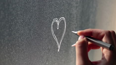 close-up of a hand drawing a heart on a dark surface