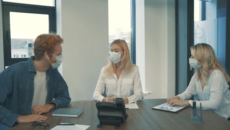 얼굴 마스크를 쓴 젊은 여성과 남성이 사무실에서 비즈니스 전화를 받고 있습니다.