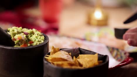 a hand reaches for tortilla chips with guacamole in a cozy, warmly lit restaurant setting