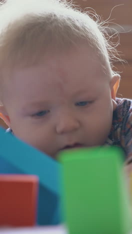 surprised little baby in warm shirt looks at tower of color cubes on soft bed in light children room close view