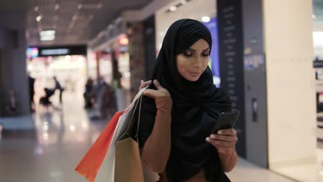 Attractive-Muslim-Woman-Wearing-Black-Hijab-Headscarf-Walking-In-The-Shopping-Mall-And-Using-Smartphone