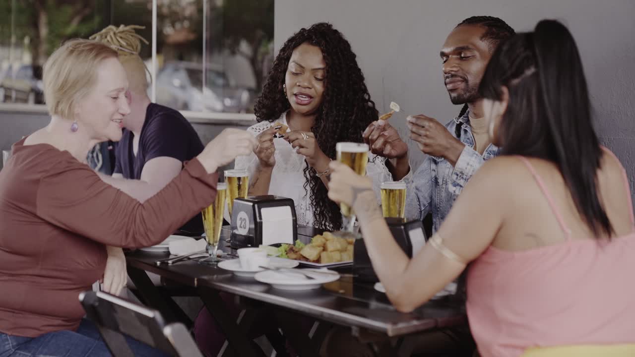 Diverse Group of Friends Enjoying Drinks and Food at an Outdoor Restaurant