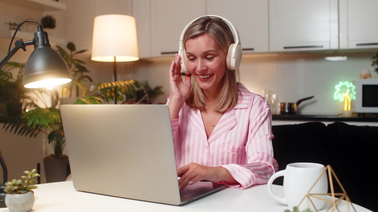Voksen, kvindelig freelancer redigerer layout på bærbar computer med hovedtelefoner på, smiler, nikker til musikken og har et stabilt workflow