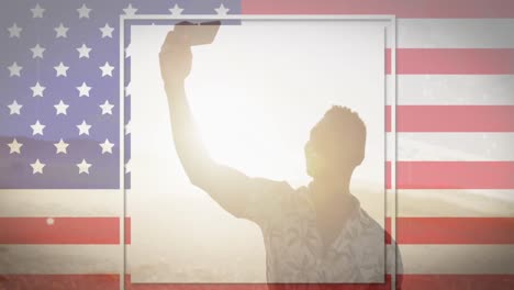 American-flag-with-glitch-effect-against-african-american-man-taking-a-selfie-at-the-beach