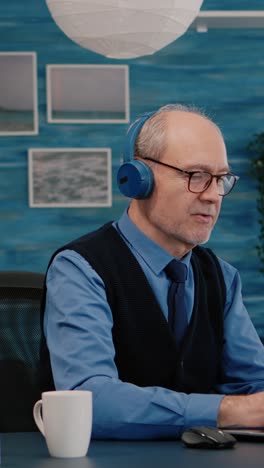 vertical video: focused old entrepreneur with headphones listening music typing on laptop
