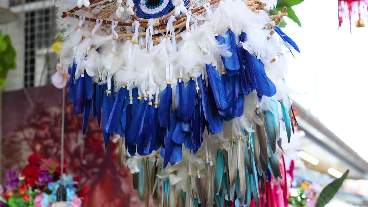 un móvil de plumas con tonos azules, blancos y rosados se balancea suavemente en un entorno brillante y floral con iluminación natural