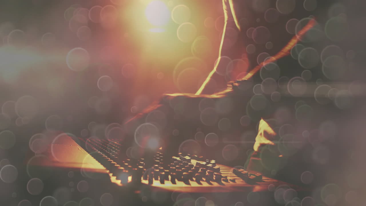 Man playing MIDI controller in dim music studio, laptop glowing with warm backlight flares
