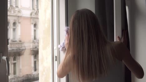 vista posterior de la mujer limpiando la ventana con un trapo mientras hace el trabajo de limpieza en casa