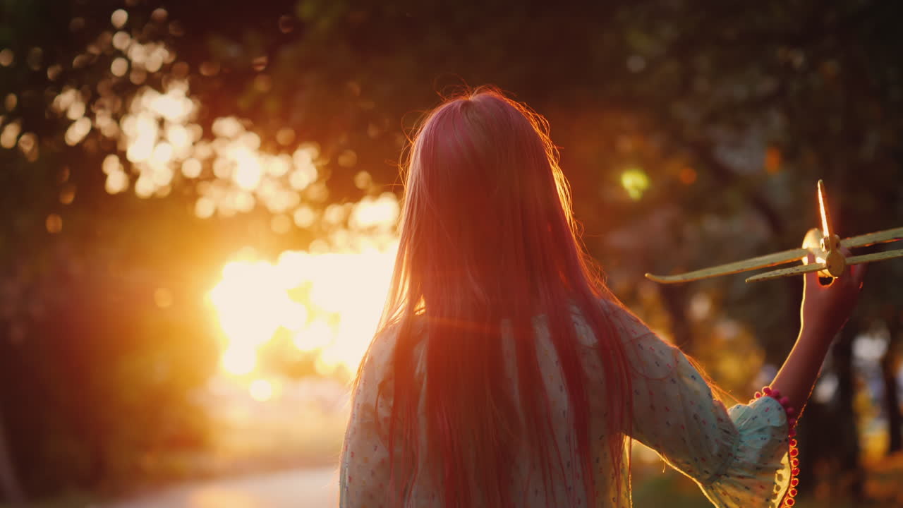 силуэт девочки с игрушечным самолетом, играющей в лучах заходящего солнца на улице