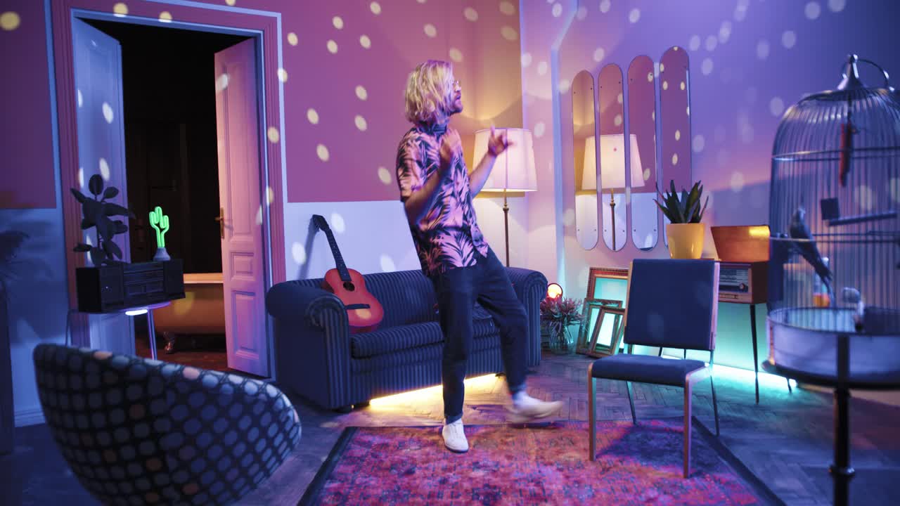 집에서 복고풍 파티에서 정력적으로 춤을 추는 안경에 긴 머리를 가진 젊은 세련된 백인 남자