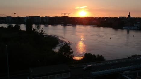 Majestuosa-Puesta-De-Sol-Sobre-La-Silueta-De-La-Ciudad-Mientras-Los-Autos-Conducen-Sobre-El-Puente,-Vista-Aérea-De-Drones