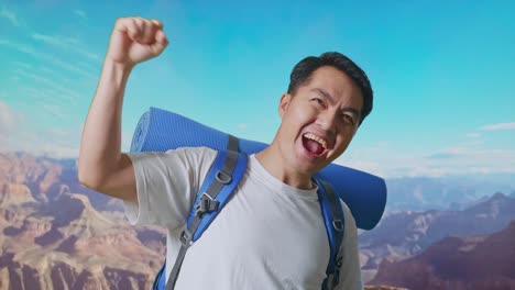 close up of asian male hiker with mountaineering backpack screaming goal celebrating the success while traveling at the top of mountain