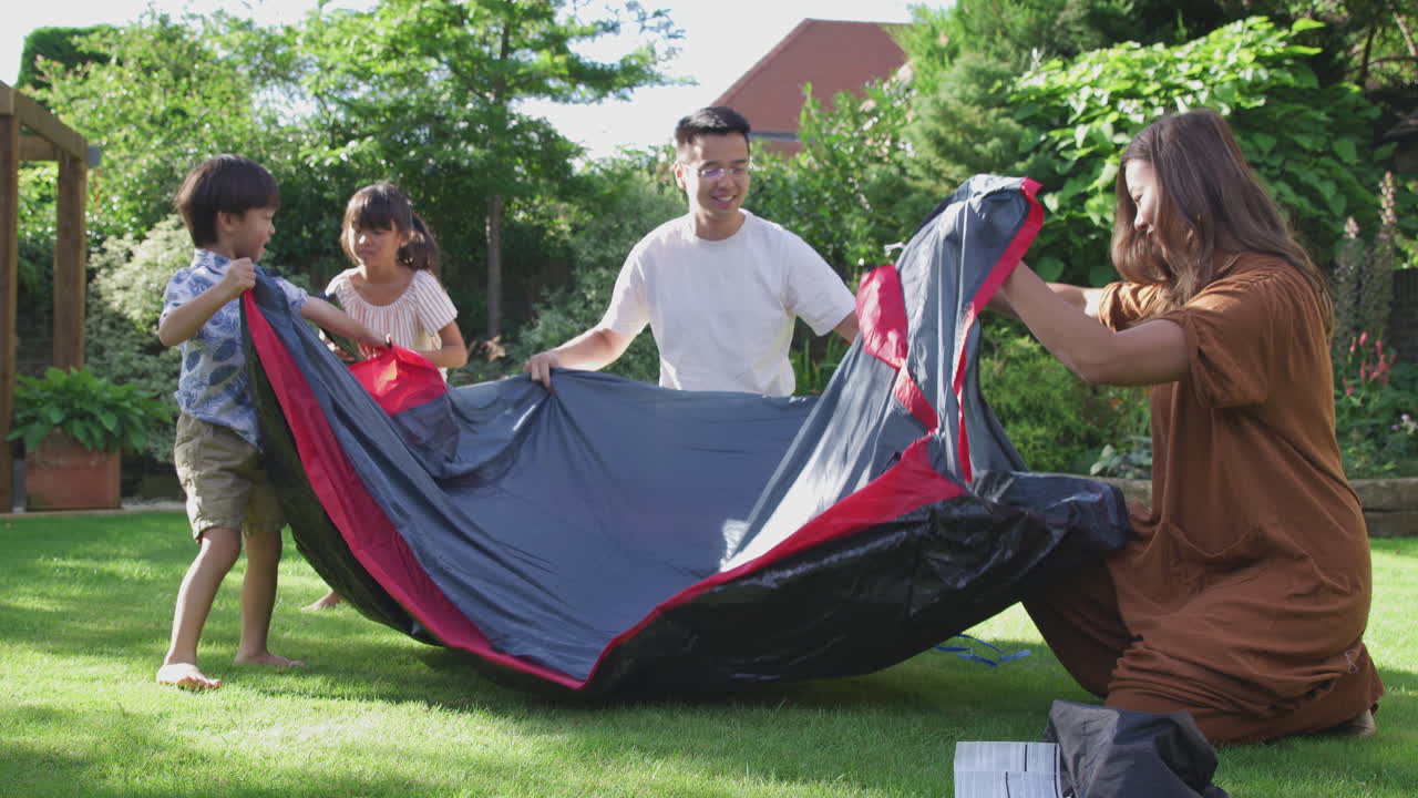 familia asiática divirtiéndose en el jardín en casa montando una tienda de campaña para un viaje de acampada de verano juntos