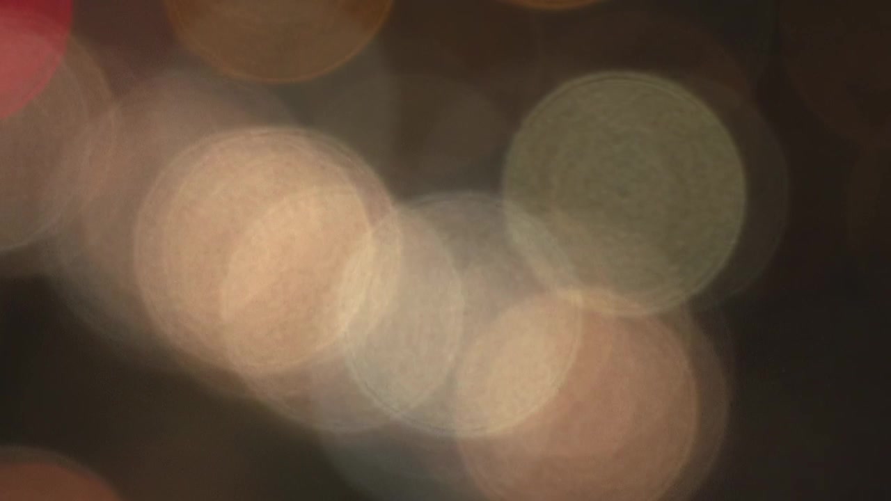 Close defocused view of moving car lights at night, creating soft circular bokeh in warm white, amber, red and green tones. Abstract urban traffic background filmed in Sofia, Bulgaria.