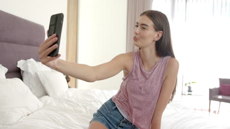 teenage caucasian girl takes a selfie, winking playfully at her phone at home