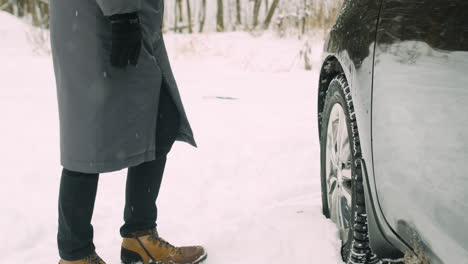 hombre revisando las ruedas del auto durante un día de invierno cubierto de nieve