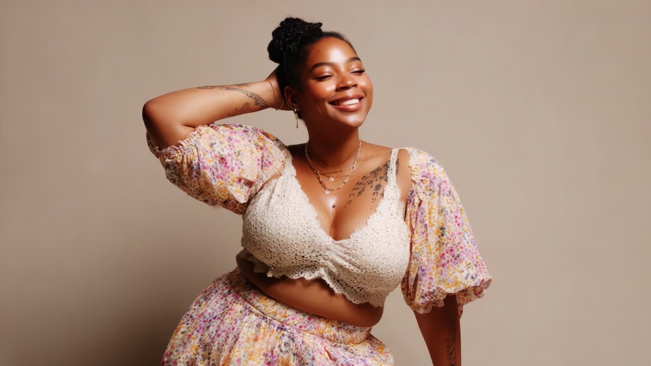 A joyful and confident woman poses gracefully in a stylish floral outfit, showcasing her radiant smile and expressive energy in a soft, neutral background that enhances her charm