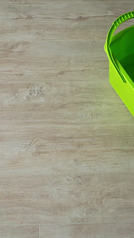 cleaning the parquet floor with a wet mop. green brush and a bucket on wooden floor. housekeeper cleans the floor with a mop. daily chores in apartment. top view. vertical video