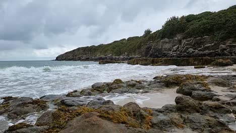 slow motion ocean waves washing over rocky coastal shoreline with woodland bay cliff curving across the skyline