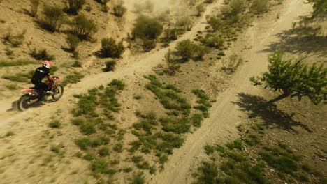 el motociclista sube a la máquina en una colina baja fpv. el deportista monta motocicletas en las tierras altas del desierto en un día soleado. viaje de ensueño en motocicleta