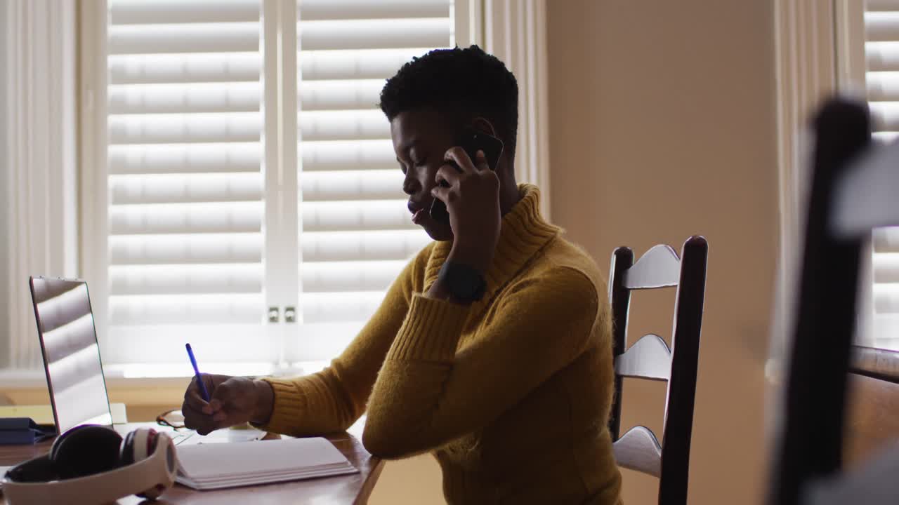 African american woman talking on smartphone and using laptop while working from home