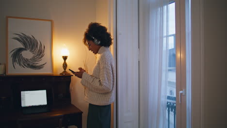 mujer relajada usando teléfono móvil ventana. auriculares mujer rizada girando música