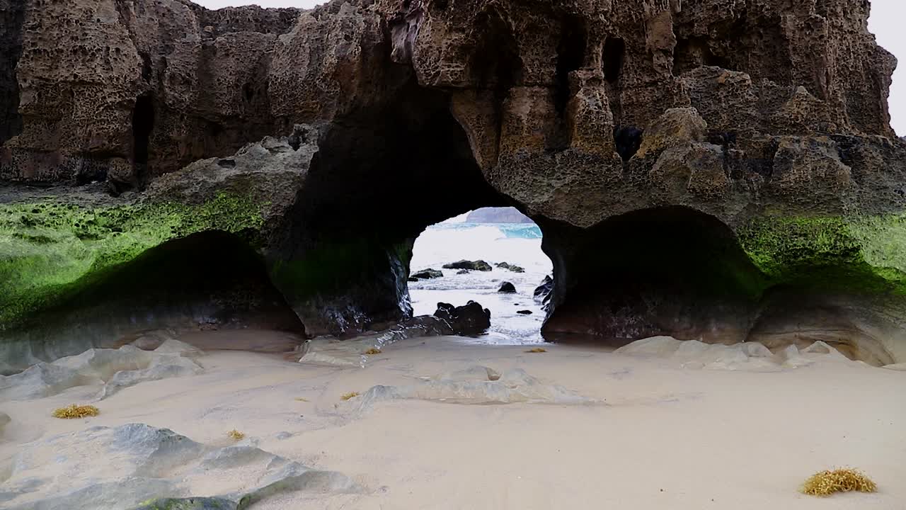 포르투갈의 포르투 산토 섬의 모래 해변에서 바다 침식으로 인한 자연 지질학 암석 섬 동굴 터널, 50fps hd 정적