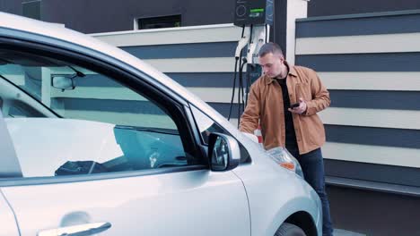 proceso de reabastecimiento de combustible de un automóvil eléctrico. un disparo debajo de la escotilla donde se carga el automóvil ecológico eléctrico. la escotella de carga del automóvil eléctrico se abre automáticamente. una mano masculina inserta un automóvil erecto
