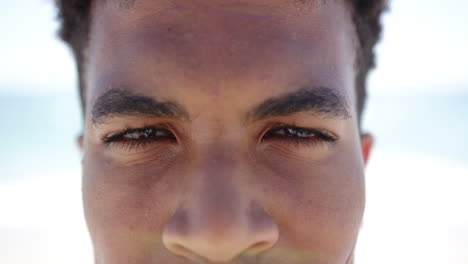 Close-up-of-a-young-biracial-man-smiling-with-a-sandy-beach-blurred-in-the-background