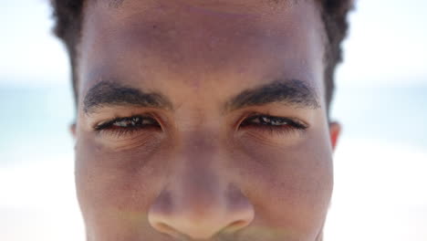 primer plano de un joven biracial sonriendo con una playa de arena borrosa en el fondo