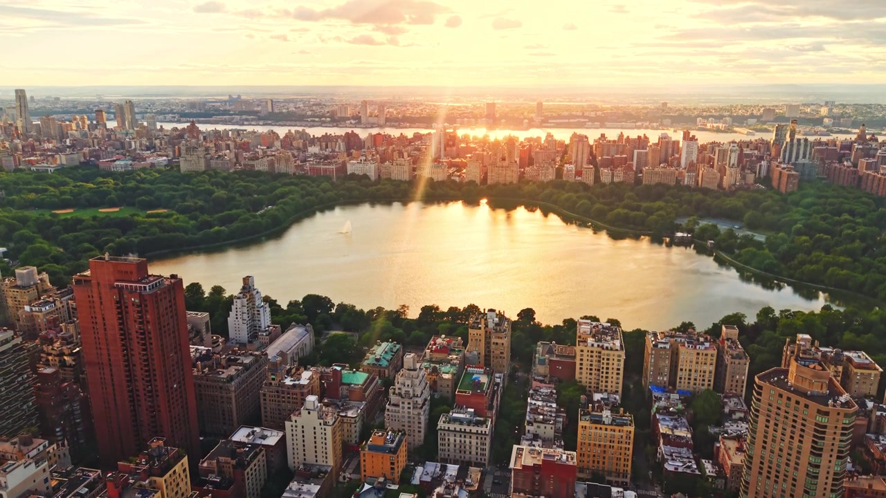 Bagliore del tramonto sul bacino idrico di Central Park, New York. Luce dorata si riflette sull'acqua circondata da alberi e condomini.