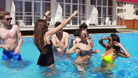 happy young cheerful friends dancing and having fun in the pool cooling off in the water on a hot summer day. summertime pool party. slowmotion shot.