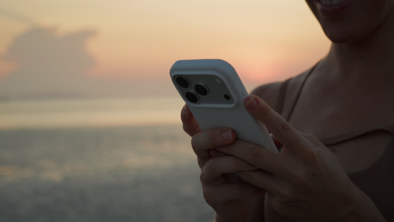 Woman's Hands Using Smartphone by the Ocean at Sunset