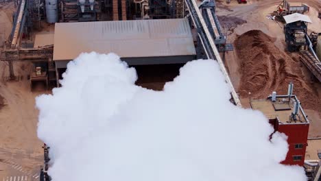 a massive industrial smoke cloud billows from factory chimney in production site