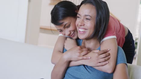 Happy-biracial-sisters-sitting-on-sofa,-and-smiling,-in-slow-motion