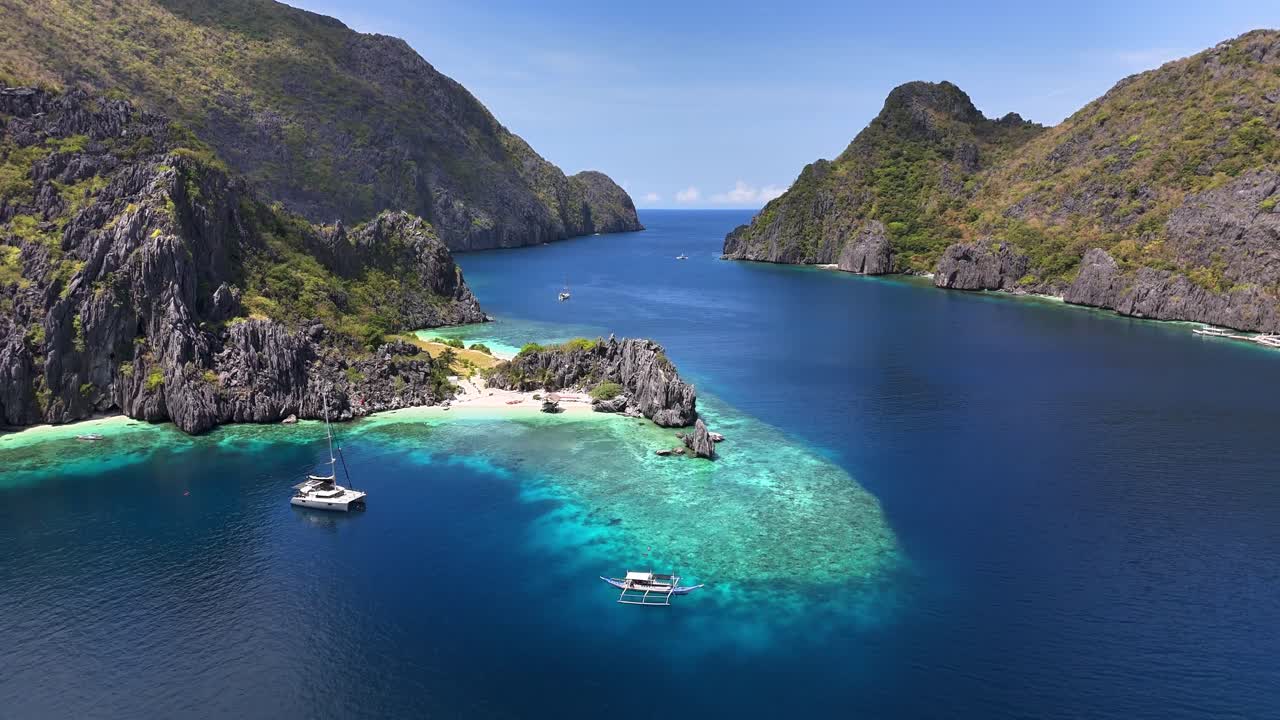 Turquoise waters surround the white sands of Star Beach on Tapiutan Island, with boats anchored near dramatic limestone cliffs and lush greenery under a bright tropical sky