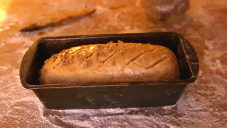 seeds being sprinkled over dough in loaf tin on a floury table