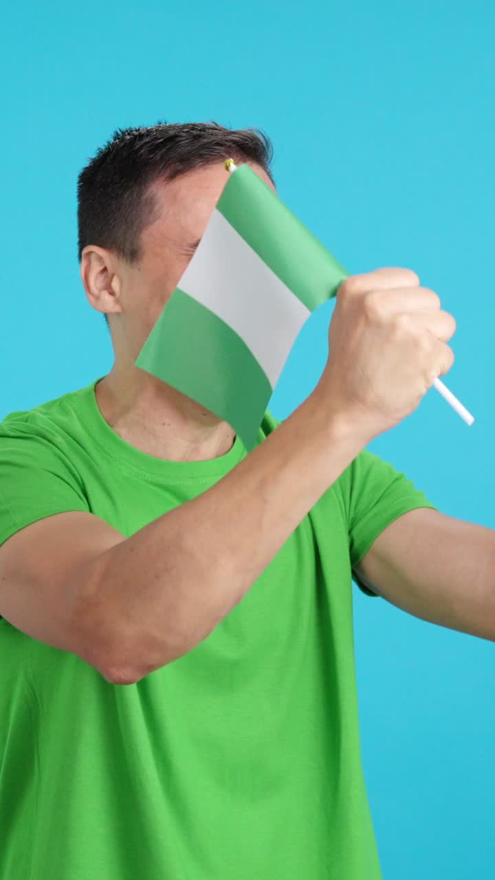 Man cheering for Nigeria waving a national flag looking away