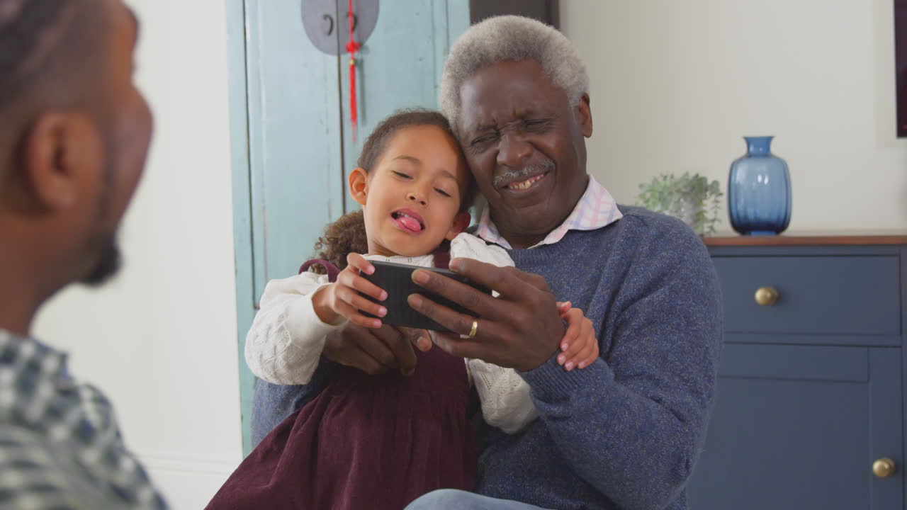 Grandfather with grandchildren playing game on mobile phone at home - shot in slow motion