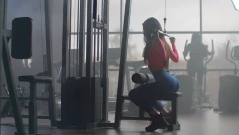 the fitness instructor girl performs power training in the gym. she pumps her back and arms for a muscular body.