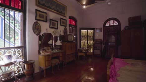 vintage furniture and appliances displayed inside the bedroom in pinang peranakan mansion in penang, malaysia with shadow of rotating ceiling fan on the wall - panoramic shot