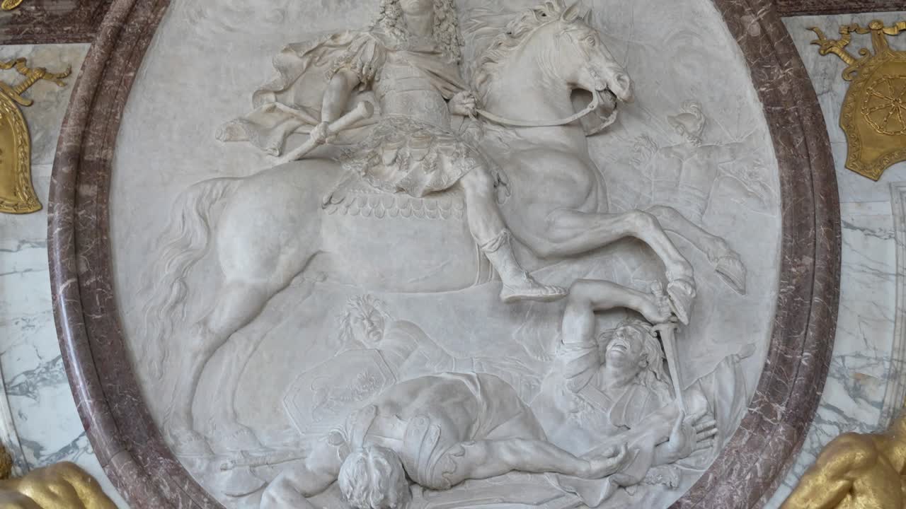 Marble relief sculpture inside Versailles Palace showing a rider on horseback surrounded by gilded decorative elements. Close view highlighting detailed craftsmanship and baroque style