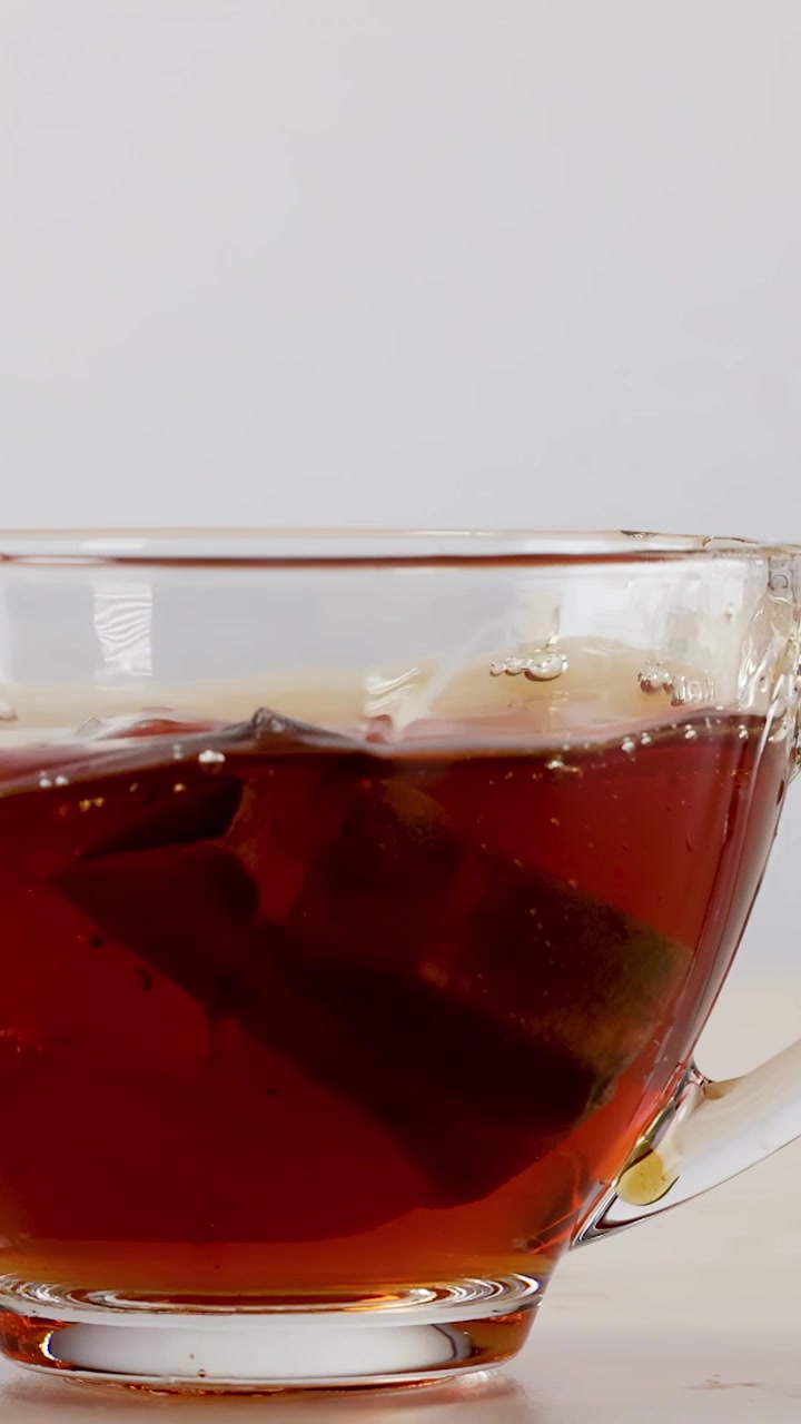 Una bustina di tè cade in una tazza di vetro, schizzando liquido caldo durante il processo di infusione.