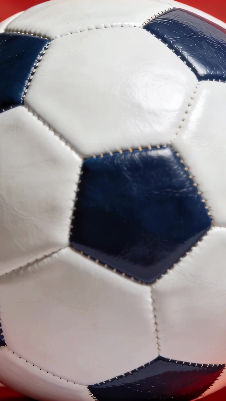 Video vertical: Balón de fútbol cosido girando mostrando las costuras después de un cambio de cámara sobre un fondo rojo